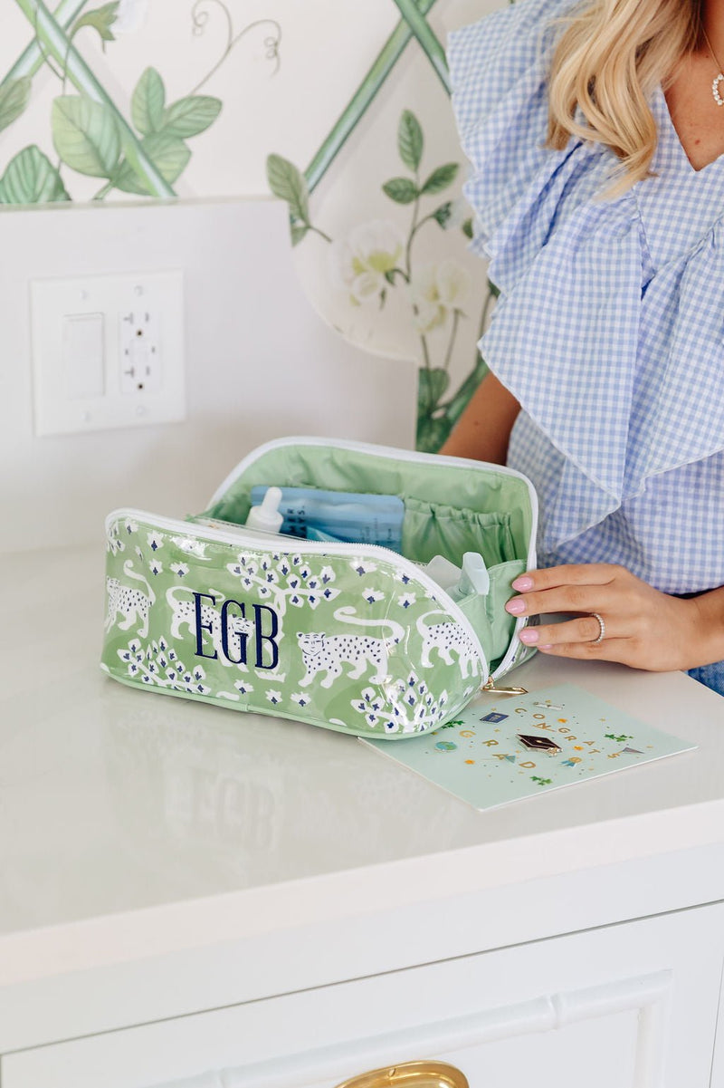 A woman unzips a green monogrammed 'EGB' flat lay pouch next to a graduation congratulations card