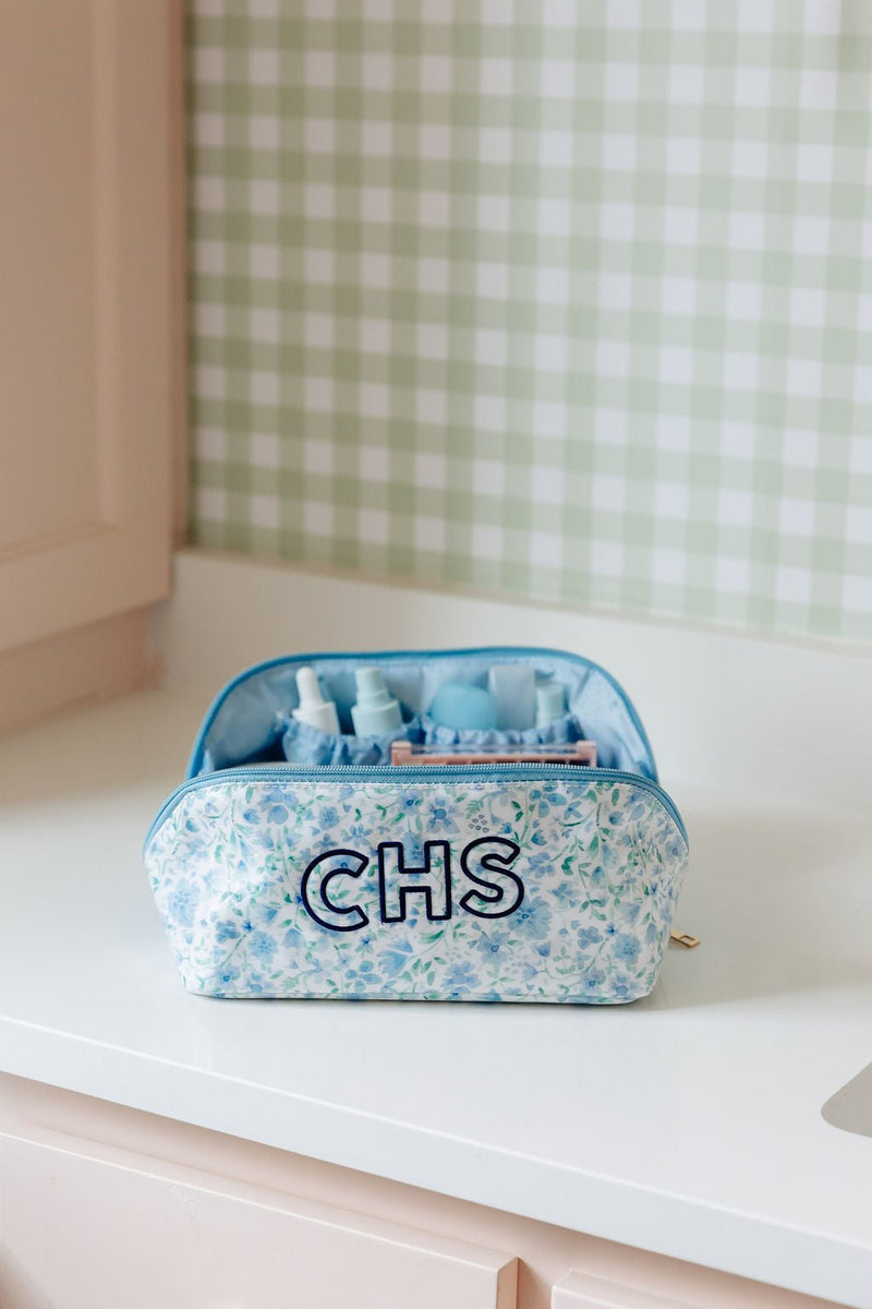 A blue floral flat lay pouch monogrammed 'CHS', open to show travel-size toiletry bottles