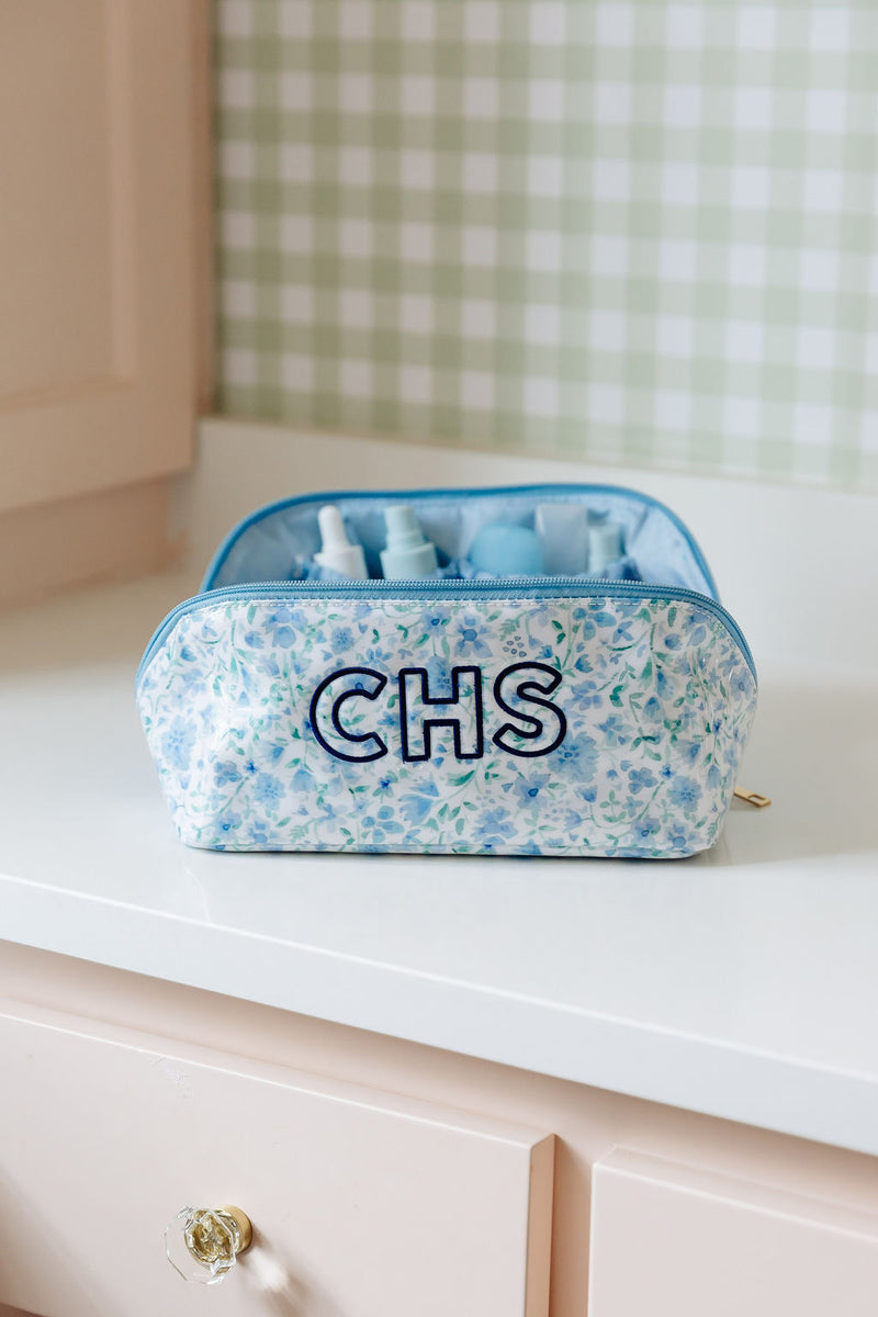 A blue floral flat lay pouch monogrammed 'CHS', open to show travel-size toiletry bottles