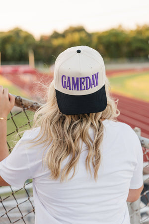 Back view on track: black-brim cap with puff purple “GAMEDAY”.