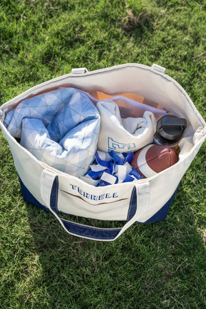 Open natural canvas tote with navy trim and embroidered “TERRELL,” filled with gameday gear (blanket, football).