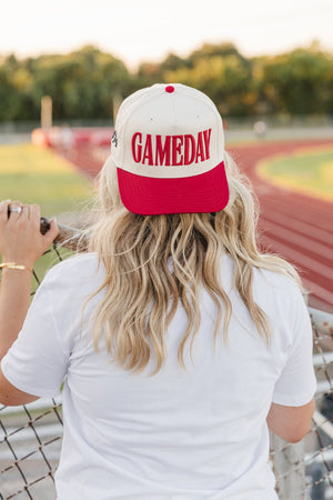 Back view at track: red-brim cap with bold puff “GAMEDAY”.