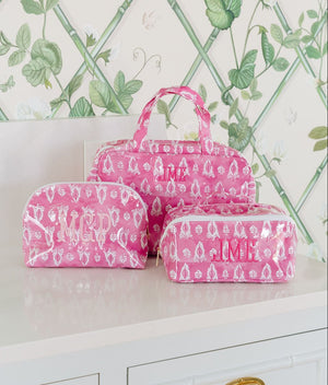 Three pink block-print bags: a hanging toiletry bag monogrammed 'JML', a dome pouch monogrammed 'MCP', and a rectangular pouch monogrammed 'JMB'