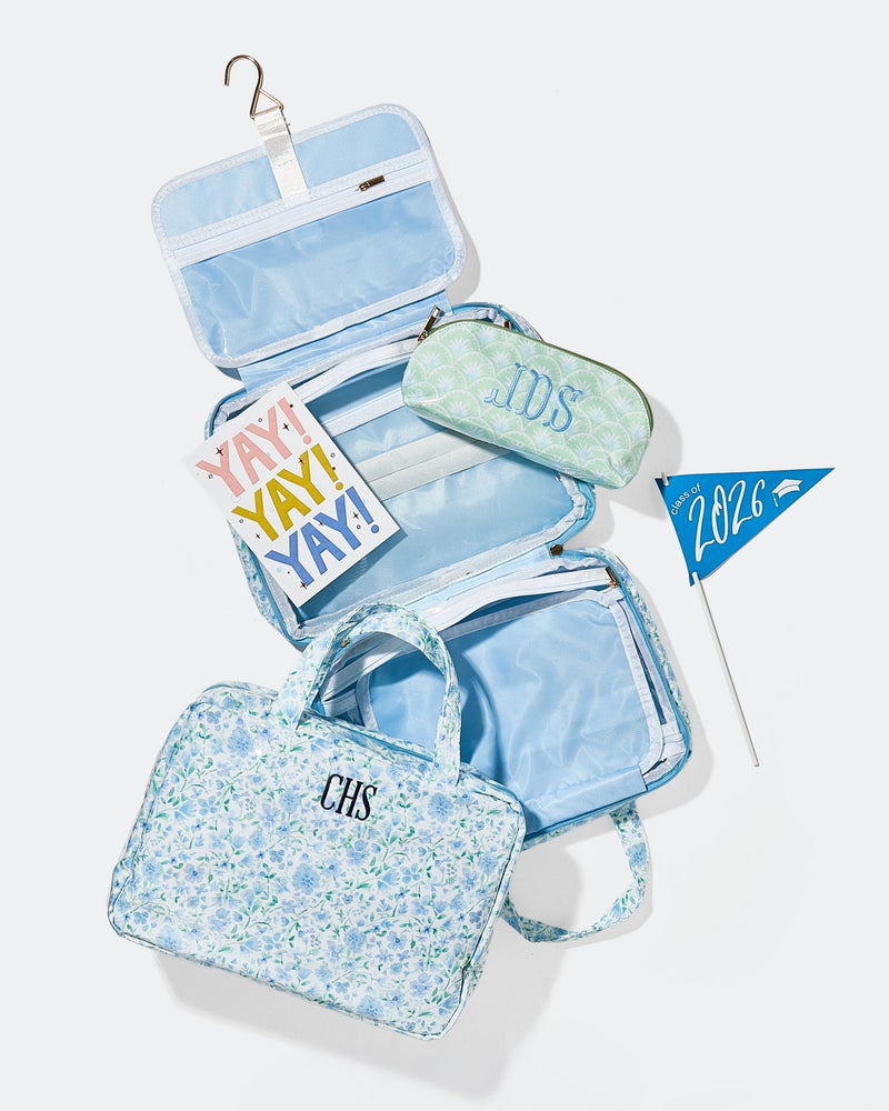 A blue floral hanging toiletry bag monogrammed 'CHS' open to show compartments, with a matching pouch monogrammed 'IDS' and a 'Class of 2026' graduation pennant