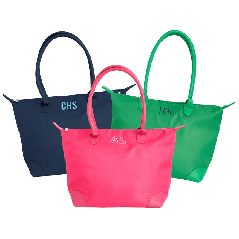 Three totes in navy monogrammed "CHS," pink monogrammed "AL," and green monogrammed "EGB," on a white background