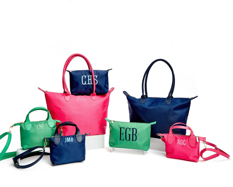 Collection of Haven totes, crossbody bags, and pouches in pink, green, and navy, monogrammed with various initials, arranged together