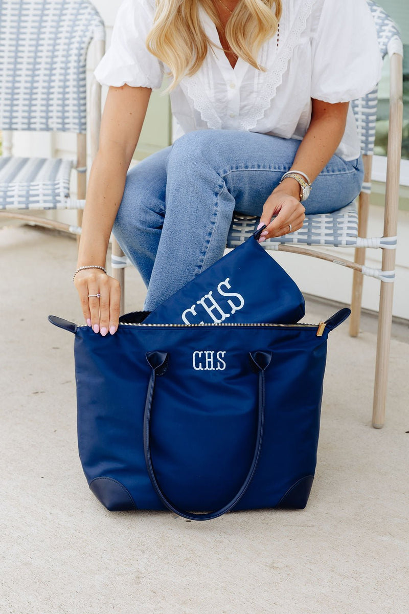 Woman zipping a navy zip pouch monogrammed "CHS" in white into a matching navy tote monogrammed "CHS"