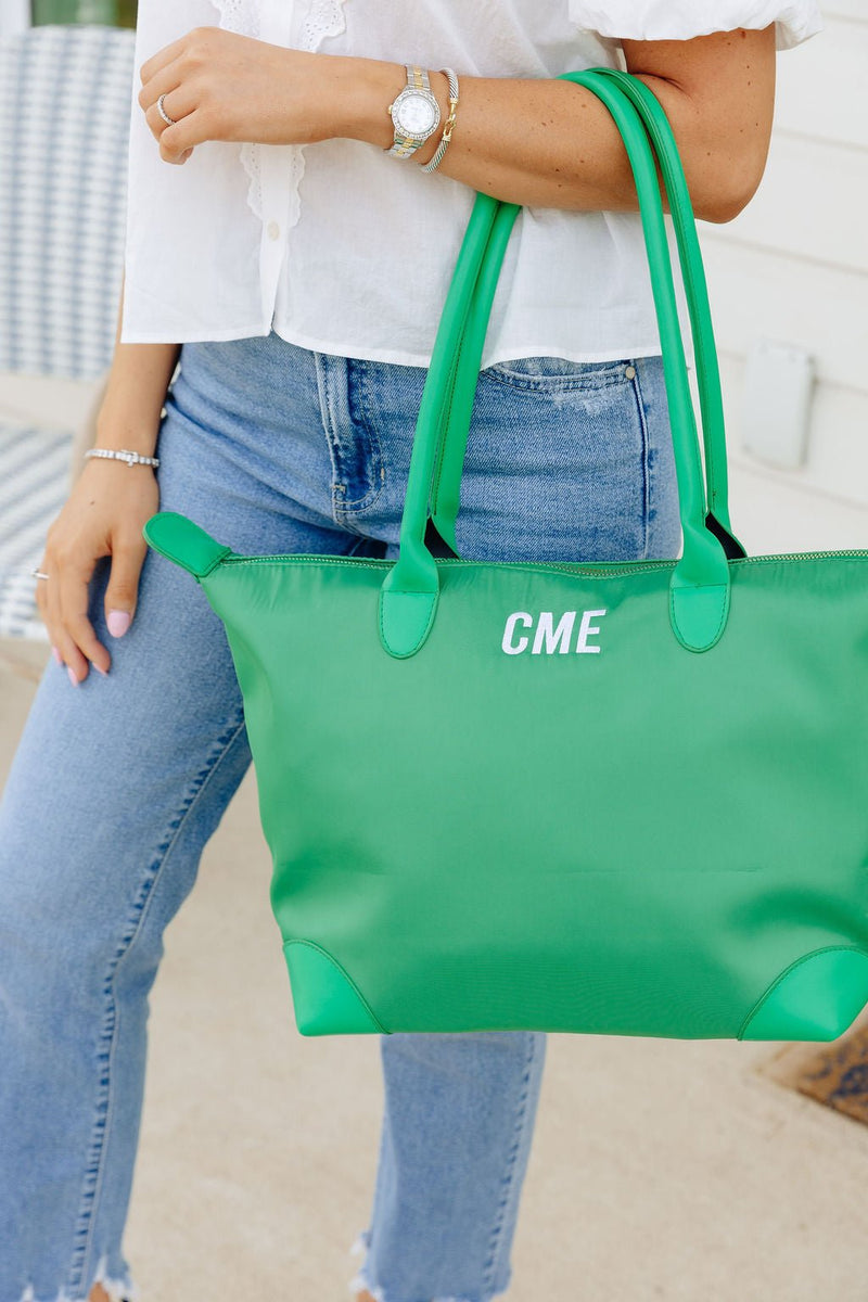 Close-up of a woman carrying a green tote monogrammed "CME" in white