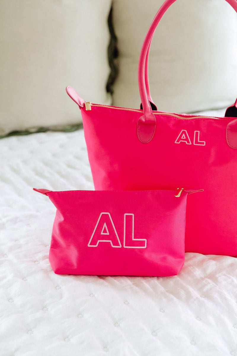 Pink tote monogrammed "AL" in white, with a matching pink zip pouch monogrammed "AL," on a bed