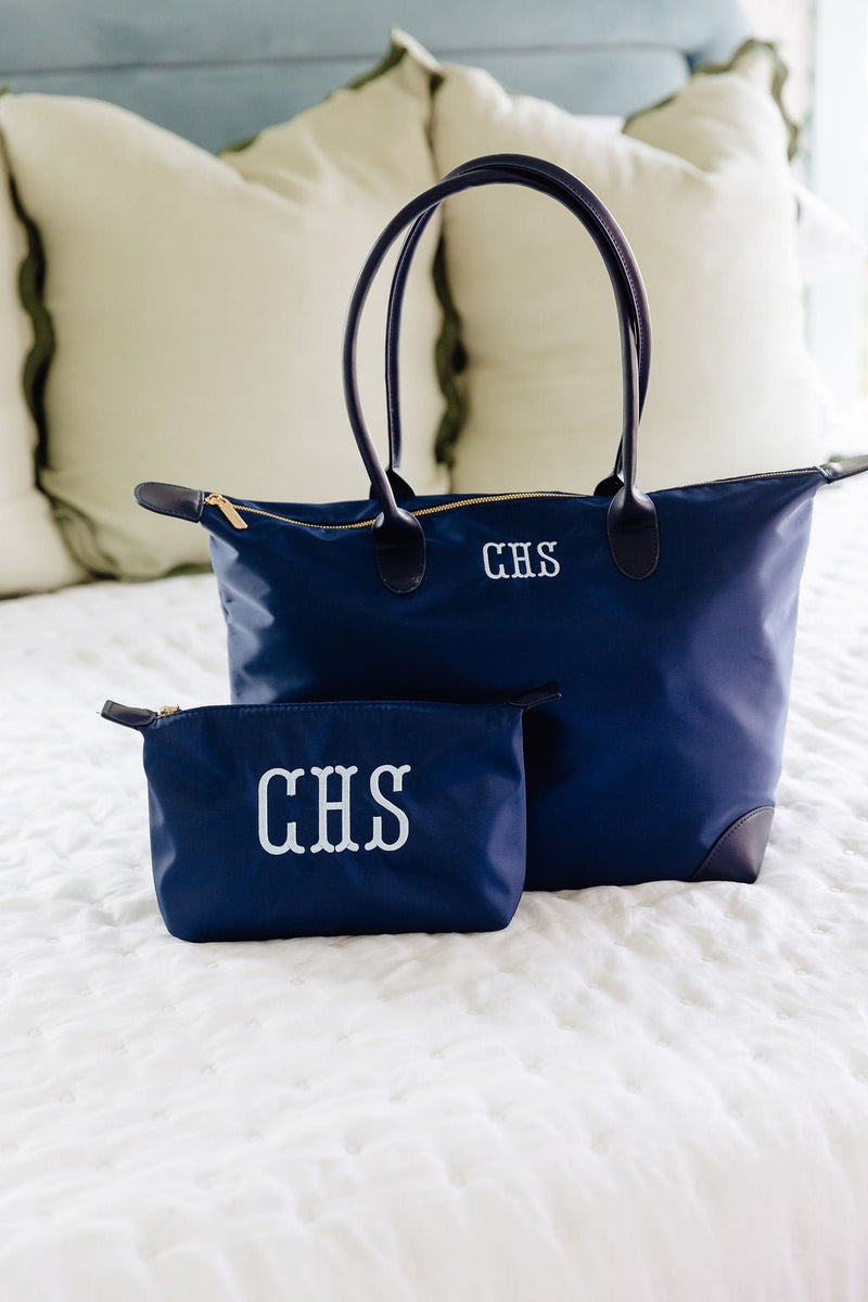 Navy tote monogrammed "CHS" in white, with a matching navy zip pouch monogrammed "CHS," on a bed