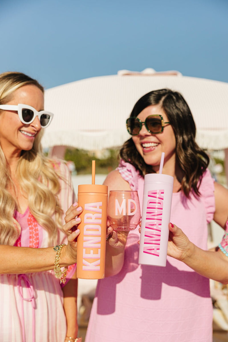Two women holding personalized drinkware, custom tumblers and wine glass with bold monogrammed names.
