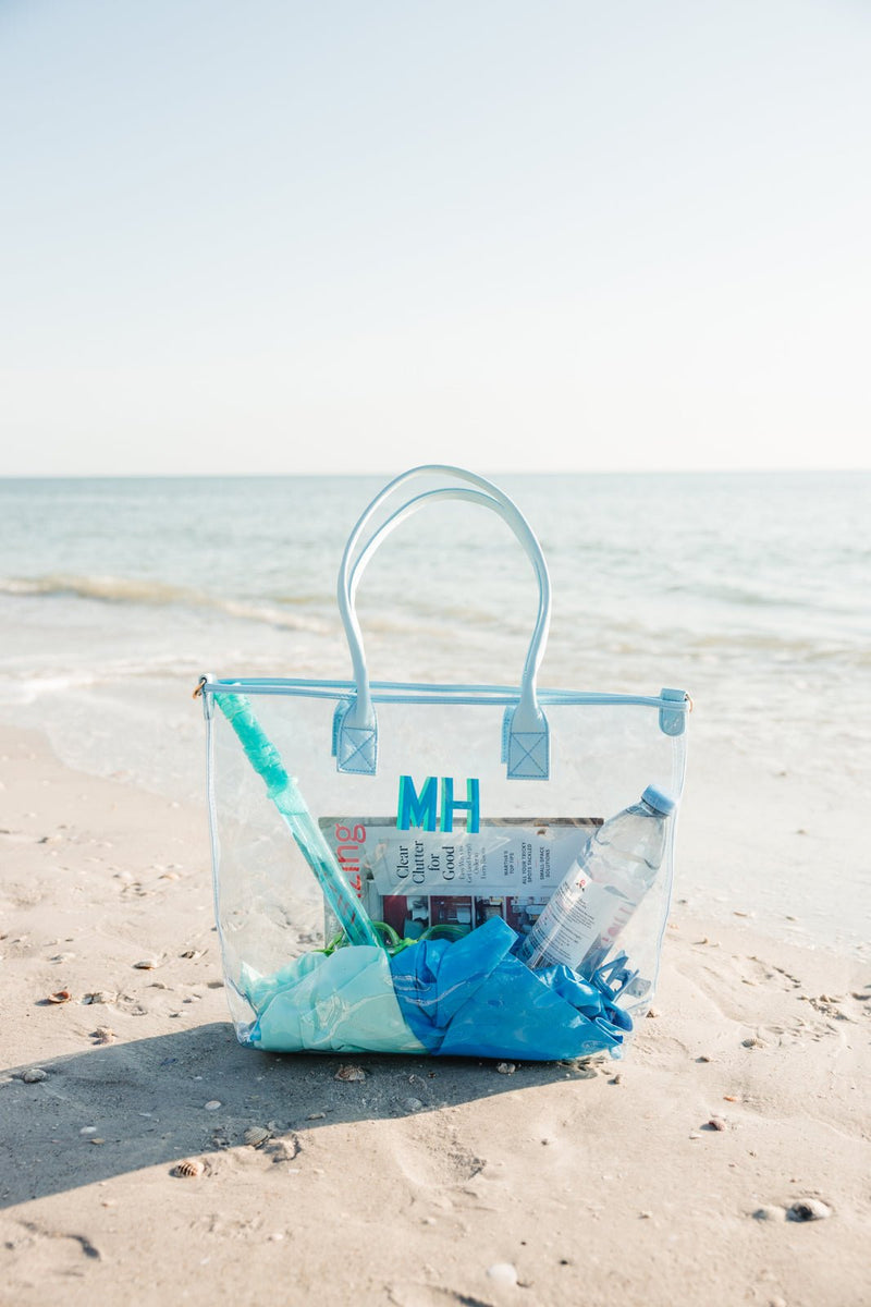 Clear monogrammed tote bag displayed on the beach with a blue design, perfect for summer outings.