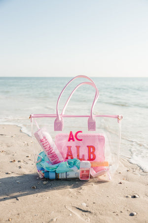 Pink monogrammed clear tote bag styled by the shore, ideal for poolside or beach trips.