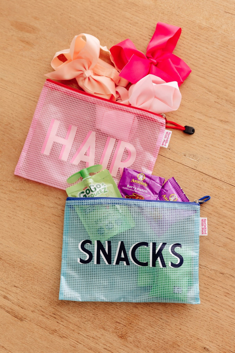 A pink mesh bag labeled Hair filled with hair bows, next to a blue mesh bag labeled Snacks filled with snack pouches