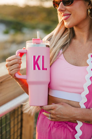 A girl in a pink outfit holds up a pink monogrammed 40 oz tumbler