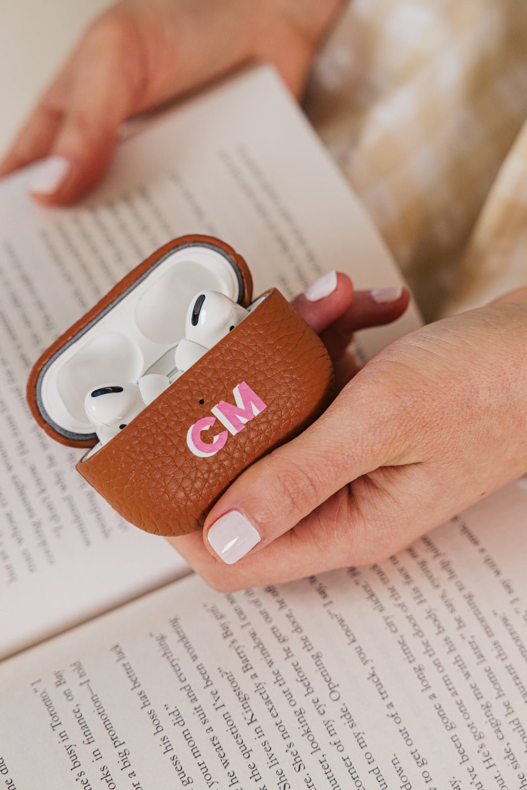 A stylish set of personalized leather AirPods cases in black and tan, designed for sleek and functional protection. The black case, featuring the initials "HF" in pink, provides a classic and sophisticated look, while the tan case, embossed with "LB" in blue, offers a warm and timeless feel. The tan case is shown open, revealing a pair of AirPods inside. These monogrammed cases are part of a coordinated travel accessories collection, perfect for gifting or adding a personalized touch to everyday tech essent