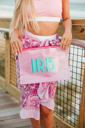A girl on a boardwalk holds up a pink pool bag with a mint and turquoise monogram.