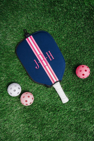 A navy and pink paddle cover is customized with an embroidered monogram and placed next to some pickleballs