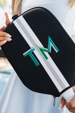 A woman holds up a black paddle cover with a blue and green embroidered monogram.