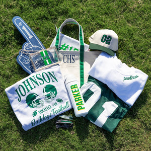 Clear stadium bag with green-white-green stripe, bold “GB” monogram on front, and gold chain shoulder strap.