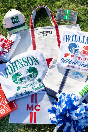 Green-striped clear stadium bag with “GB” monogram and gold chain strap displayed among gameday gear.