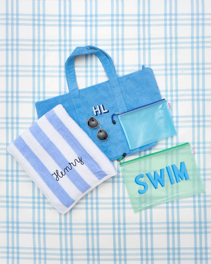 Personalized swim gift bundle set featuring a monogrammed blue terry tote bag, striped beach towel with 'Henry' embroidery, mesh pouches labeled 'SWIM', and sunglasses, styled on a blue plaid background—perfect for pool or beach days.