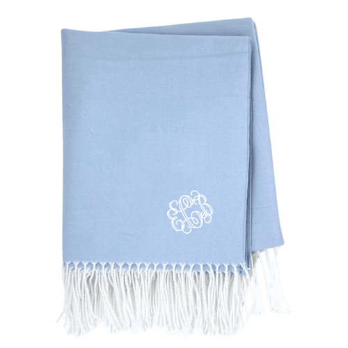 Folded light blue woven blanket with fringe trim, monogrammed in white in the corner.