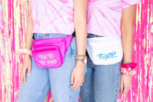Two girls in jeans and pink tie dye shirts wear a customized pink and a white fanny pack.