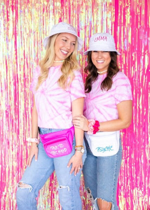 Two girls in jeans and pink tie dye shirts wear a customized pink and a white fanny pack.