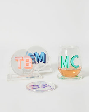 Multiple coaster sets are laid out by a wine glass to show off their custom monograms in different colors.