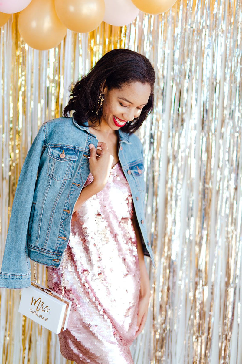 A woman in a pink sequin dress holds a customized white clutch