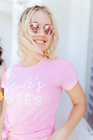 A blonde wears a light pink tee that reads "bride's babes"