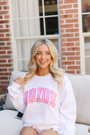 A blonde wears a light pink sweatshirt with "Bride" written on the front in pink