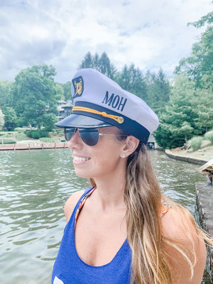 A woman in a blue tank top wears a monogrammed captain's hat