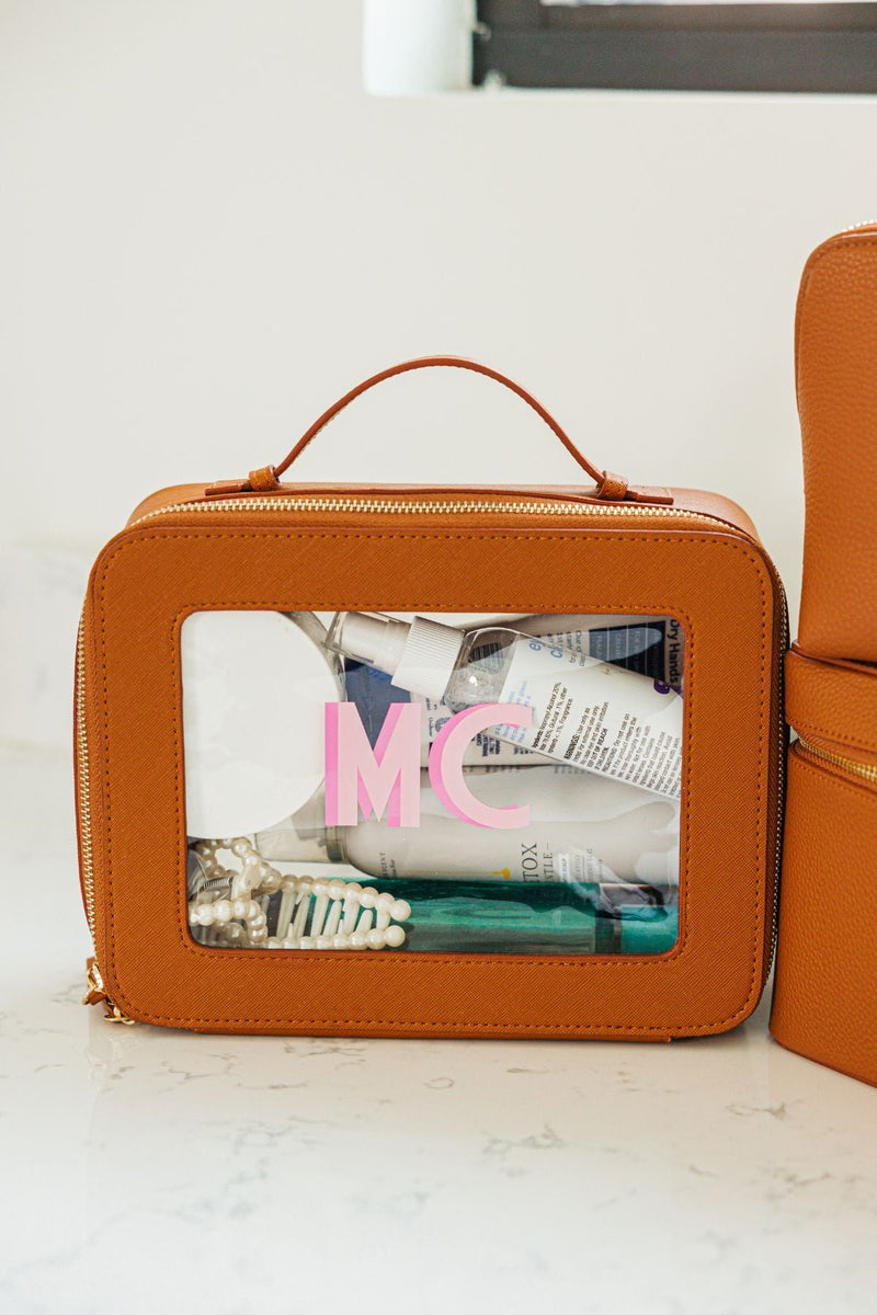 A tan leather toiletry case is personalized with a large pink monogram.