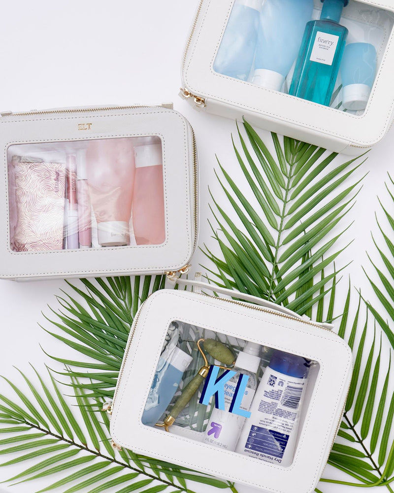 A group of white clear leather toiletry pouches are monogrammed.