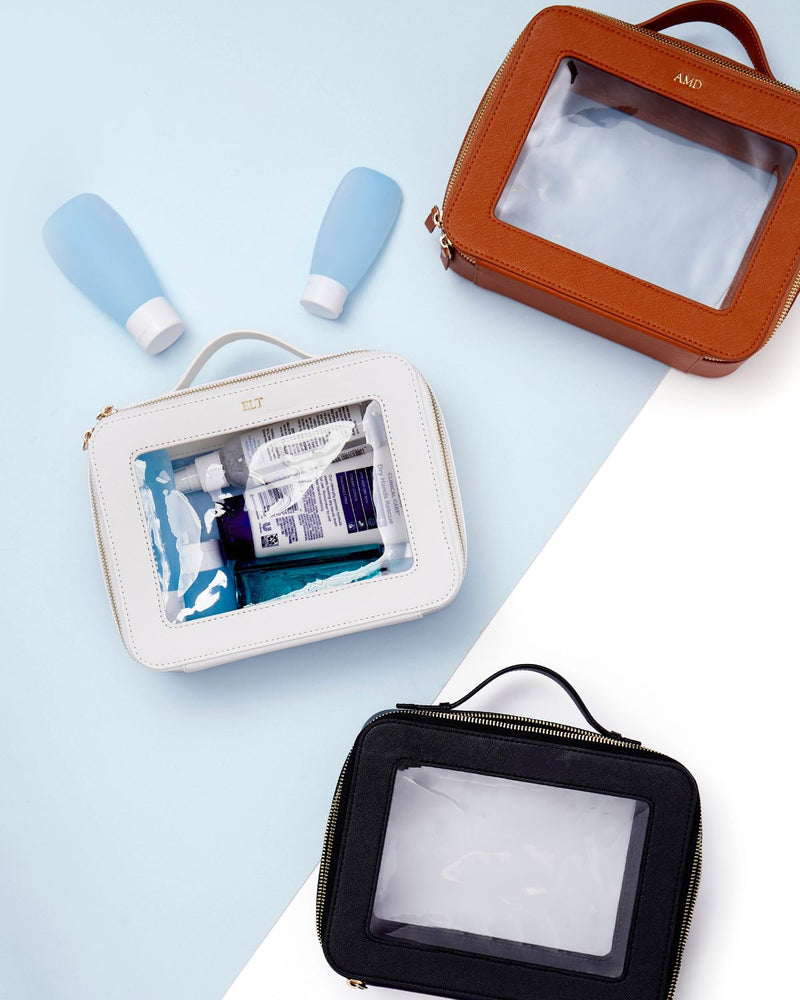 A group of white, tan, and black train cases are personalized with gold metallic monograms.