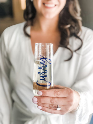 A woman holds up a champagne flute personalized with her name in navy script font.