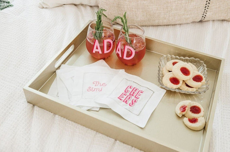 A tray with an assortment of pink cocktail napkins and a monogrammed wine glass.