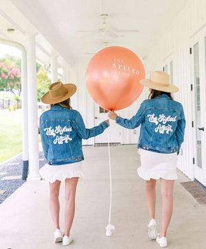 Two women stand with a big balloon showing off their customized jean jackets.