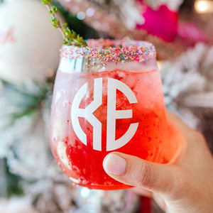 A person holds up a monogrammed wine glass filled with a red drink.