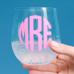 A person holds up a wine glass with a pink monogram printed on it.