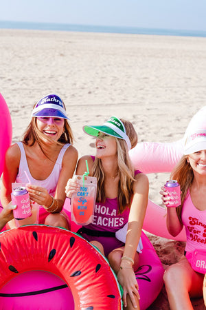 A group of girls wear customized swimsuits and visors while they drink from custom party pouches.