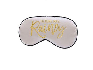 A white sleep mask is customized to read "Future Mrs. Rainey" in a gold glitter font.