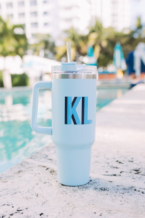 A blue monogrammed tumbler that reads "KL" sits next to a pool