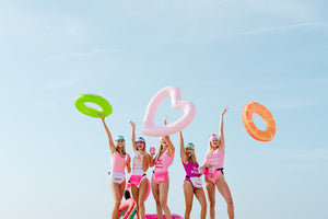 A group of girls wear custom swimsuits as they throw pool floaties in the air