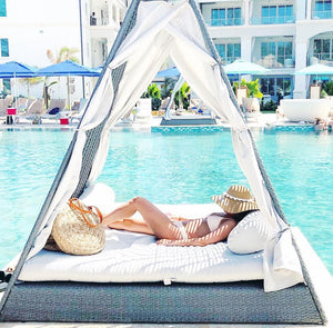 A woman relaxes poolside while wearing a floppy hat