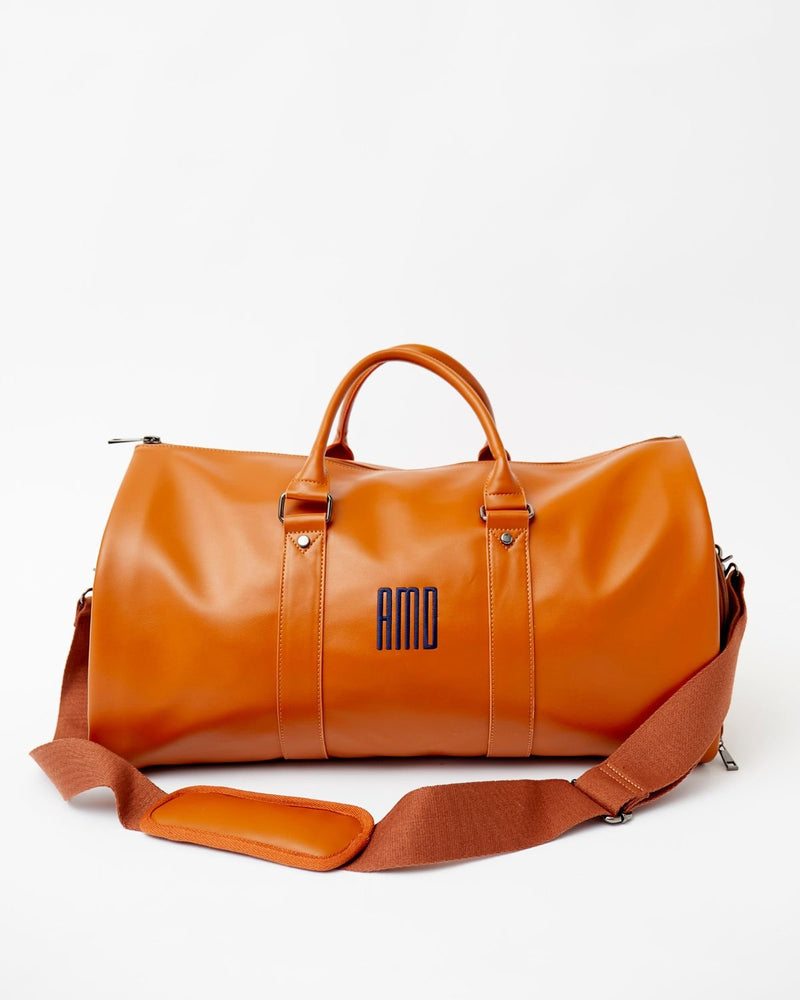 A tan duffel bag with a cross body strap is personalized with a navy monogram.