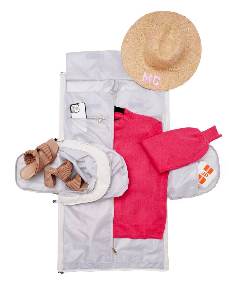 A garment bag is laid open with various clothes and travel accessories inside.