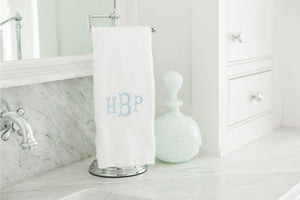 A white hand towel sits next to a sink with a classy blue monogram embroidered on the front.